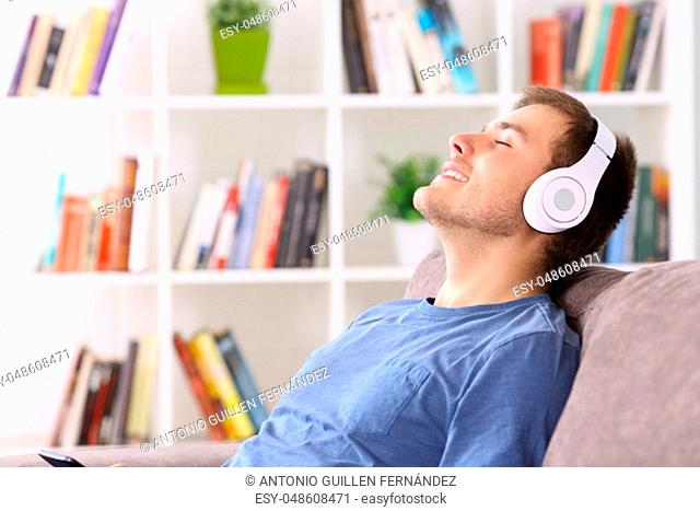 Side view portrait of a man relaxing sitting on a couch at home listening to music wearing headphones