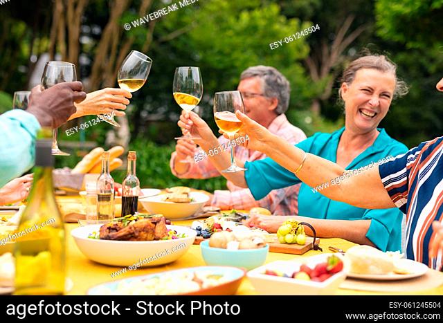 Multiracial senior male and female friends enjoying wine at table during backyard party