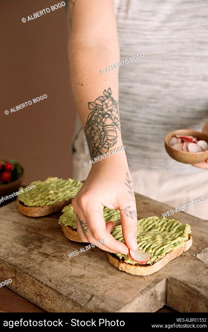 Young woman garnishing guacamole on baked bread while standing in kitchen at home