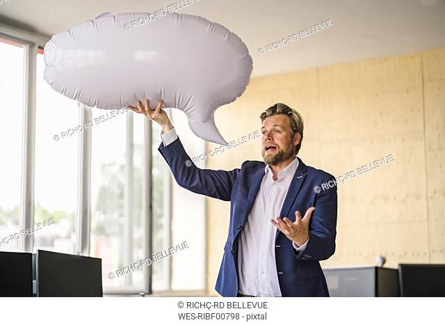 Businessman standing in office, holding inflatable speech bubble