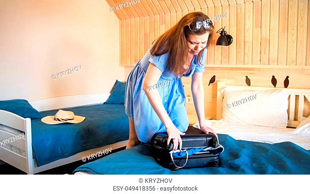 Young woman jumping on suitcase trying to close it