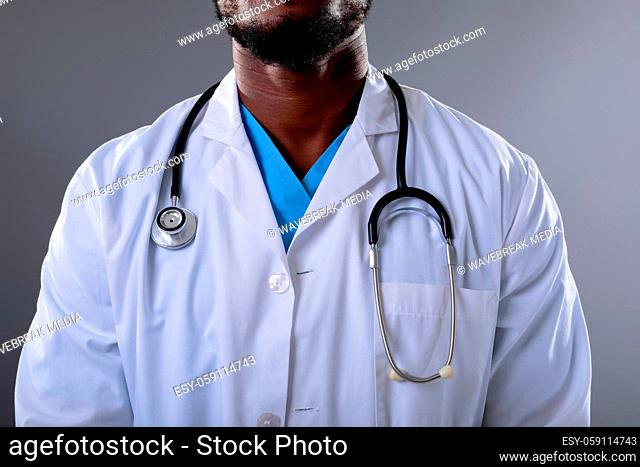 Mid section of african american male doctor wearing stethoscope against grey background