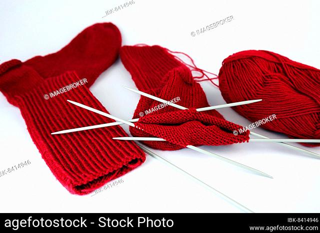 Self-knitted red socks made of wool isolated against a white background with knitting needle and ball of wool