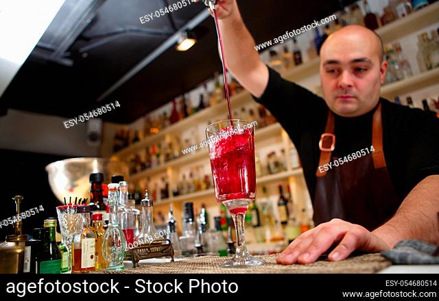 Bartender pouring red cocktail into glass at the bar