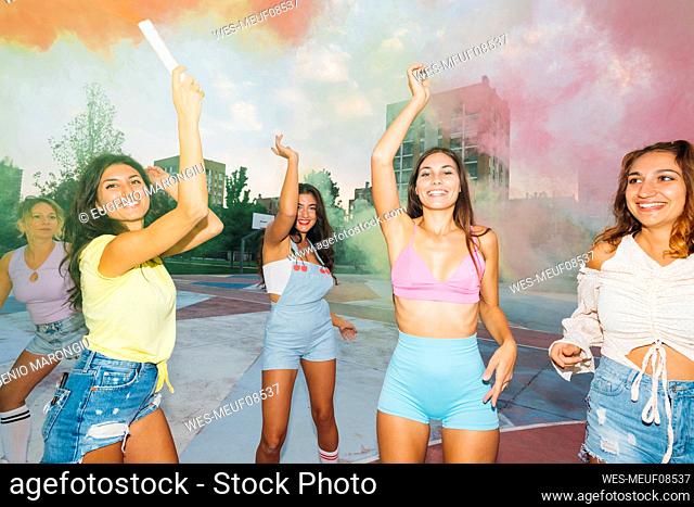 Smiling woman holding smoke torch standing with friends at sports court