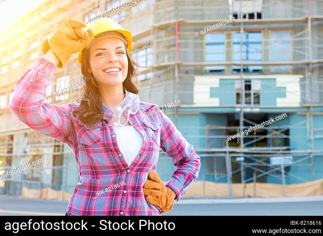 Portrait of young female construction worker wearing gloves, hard hat and protective goggles at construction site