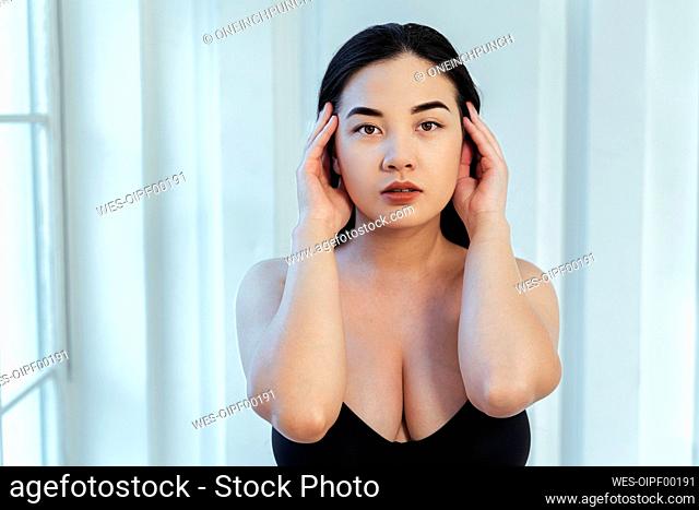 Plus size model with hand in hair wearing black bra against white wall