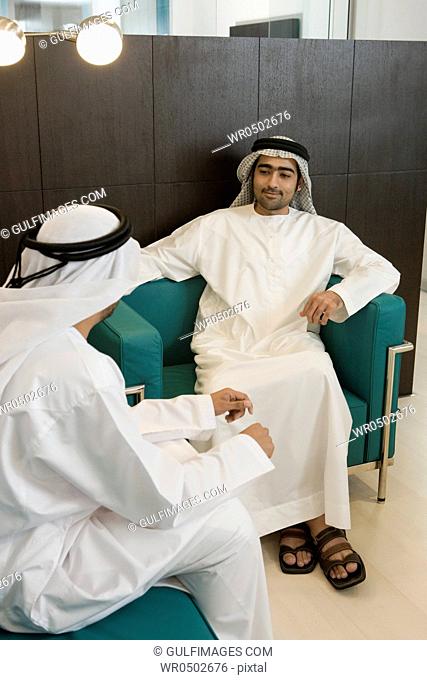 Two Arab businessmen sitting in office, discussing, smiling