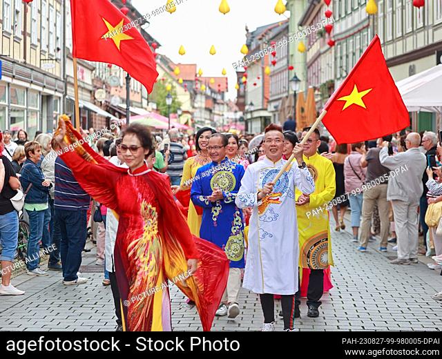 27 August 2023, Saxony-Anhalt, Wernigerode: Participants of a parade march through the old town of Wernigerode with a national flag of the socialist republic of...