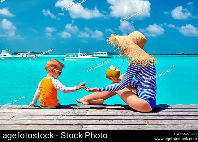 Three year old toddler boy with mother sitting on wooden jetty. Summer family vacation at Maldives