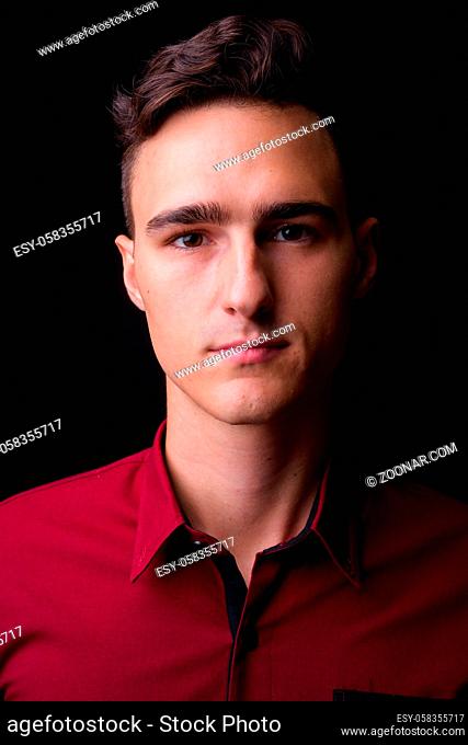 Studio shot of young handsome businessman in red shirt against black background