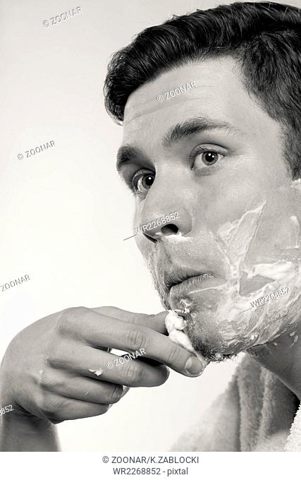 Young man shaving using razor with cream foam