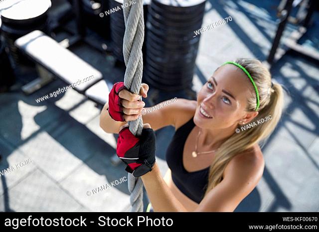 Smiling woman climbing rope at rooftop gym