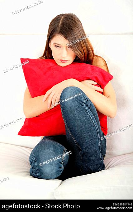 Sad woman's sitting on couch and squeezeing pillow