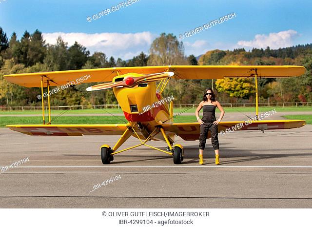 Young woman with sunglasses in overall and boots posing in front of double-decker airplane, fashion, lifestyle, photo shoot