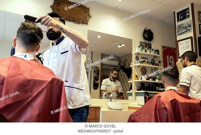 Two barbers cutting hair of twin brothers in barber shop