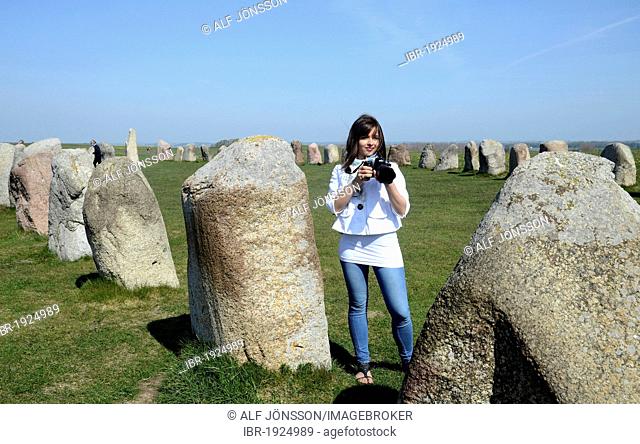Girl taking pictures at Ale's Stones, Ales stenar, Kåseberga, Sweden, Europe