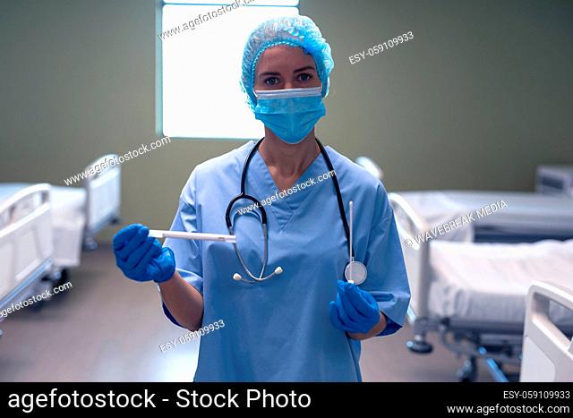 Portrait of caucasian female doctor in hospital in face mask and surgical gloves holding swab test