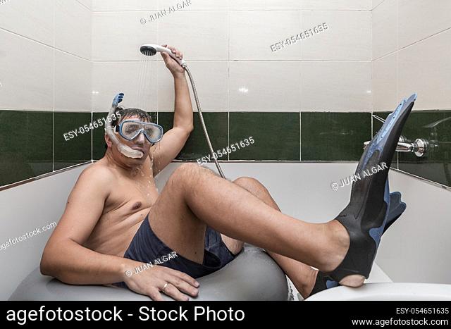 Adult man in snorkeling mask and flippers sitting on swimming ring and taking shower while pretending to rest on beach during self isolation at home