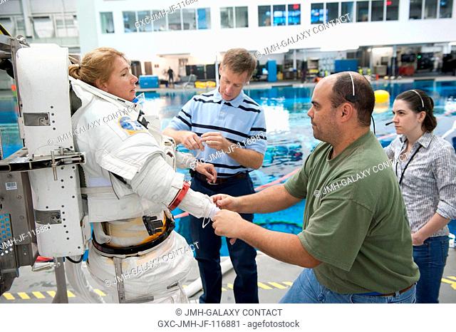NASA astronaut Sandy Magnus, STS-135 mission specialist, gets help donning a training version of her Extravehicular Mobility Unit (EMU) spacesuit in preparation...