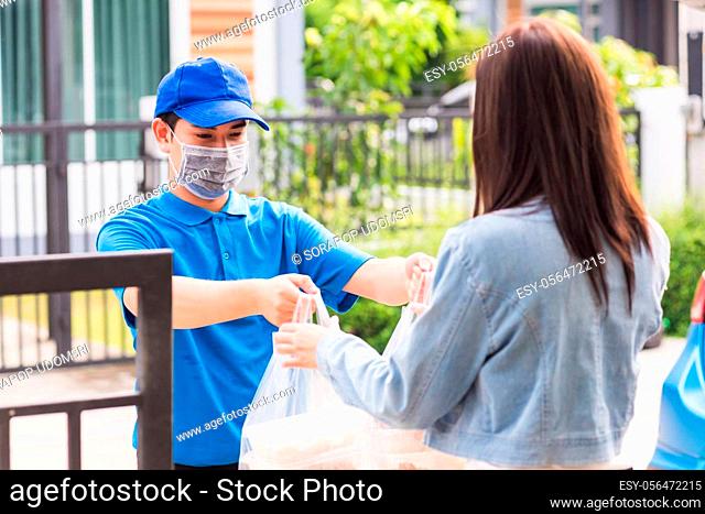 Asian young delivery man wear face mask he making grocery service giving rice food boxes plastic bags to woman customer receiving door at house after pandemic...
