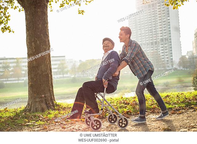 Grandson pushing happy senior man with wheeled walker