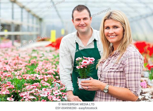 Smiling woman holding flower pot with employee in garden center