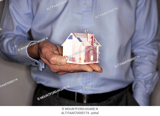 Man holding model house folded with euro banknote, mid section