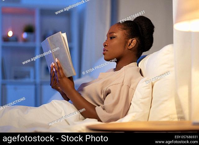 young woman reading book in bed at home