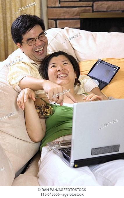 Asian couple in their 30's watching movie on laptop together having fun