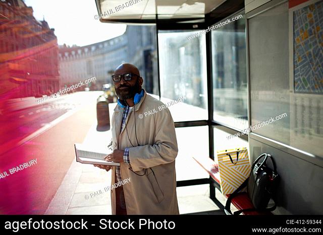 Businessman with book waiting at urban bus stop, London, UK