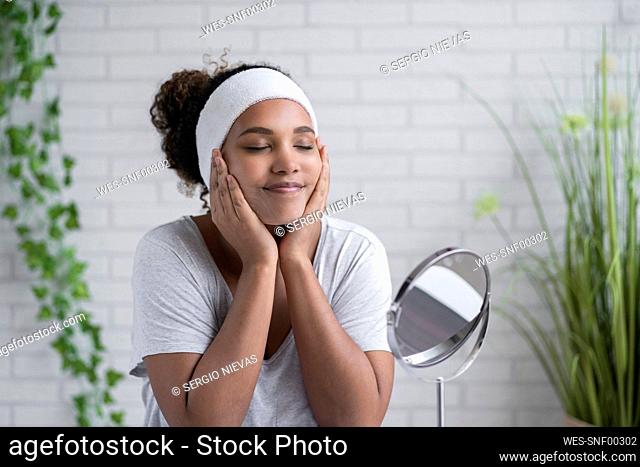 Woman with eyes closed applying cleansing foam on face at home