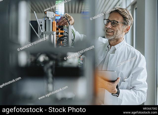 Smiling male scientist holding digital tablet inventing machinery in laboratory