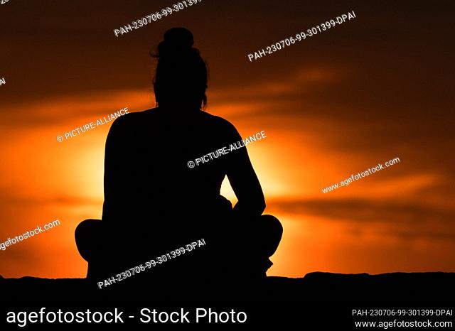 SYMBOL - 05 July 2023, Serbia, Belgrad: A woman sits on a wall at Kalemegdan Park at sunset. Thereby she can be seen as a silhouette