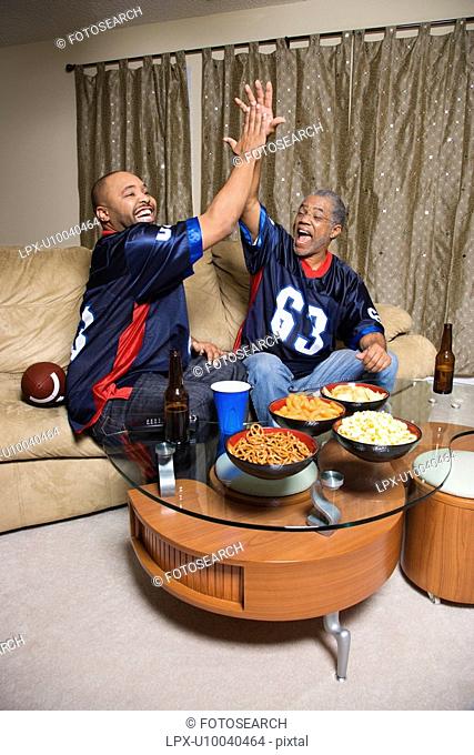 African-American father and son giving high five while watching football game