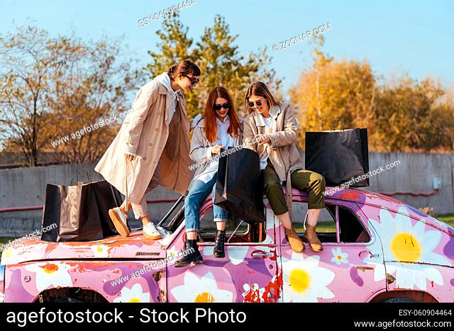 Young happy women with shopping bags posing near an old decorated car