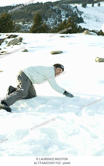 Young man down on all fours in snow, smiling, full length