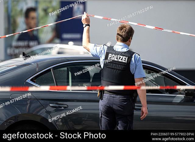 07 June 2022, Hessen, Schwalmstadt: A police officer walks under a barrier tape fixed in front of a shopping market. In the case of the fatal shooting in a...