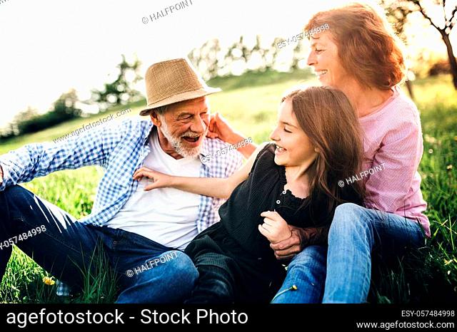 Senior couple with granddaughter outside in spring nature, relaxing on the grass and having fun