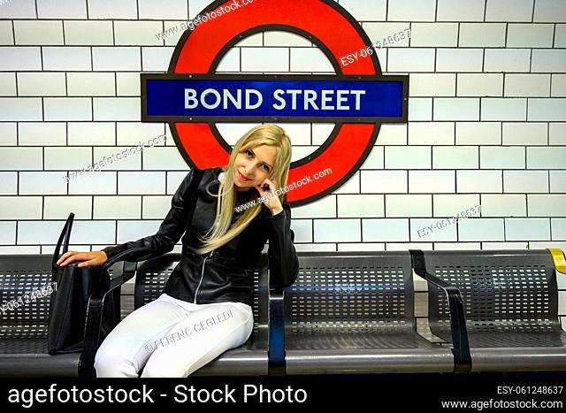 Attractive young urban woman sitting on a platform bench at Bond Street and waiting for an underground in London, United Kingdom