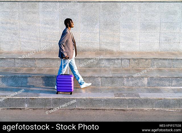 Smiling young businessman with suitcase walking on step