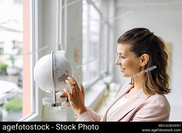 Smiling businesswoman touching globe in office