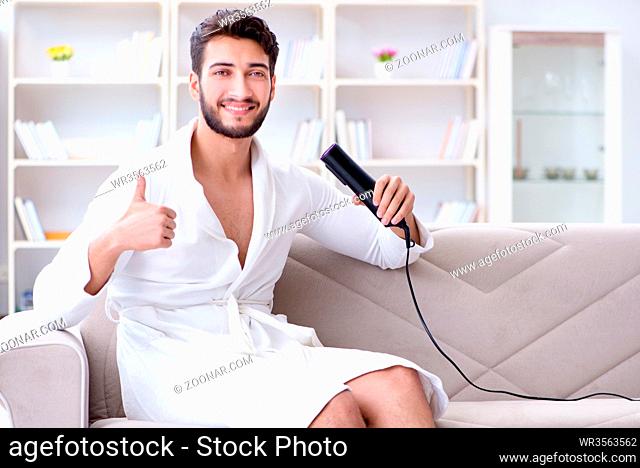 Young man drying hair at home with a hair dryer blower