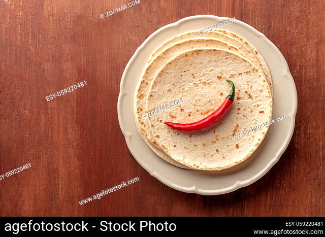 A red chilli pepper, shot from the top on a pile of tortillas, Mexican flatbreads, on a dark rustic wooden background with a place for text