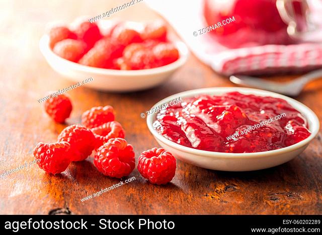 Red rasberries jam in bowl and ripe raspberries on wooden table