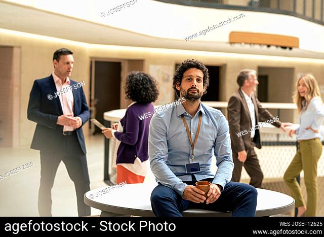 Businessman holding coffee cup with colleagues discussing in background