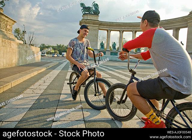 Young male BMX bikers taking break while sitting on bicycles at Hero's Square, Budapest, Hungary