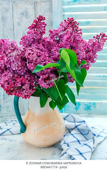 Blooming lilacs in a ceramic jug on a white table