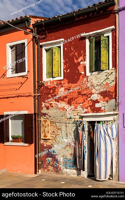 Old red stucco and brick house facade decorated with blue and white striped curtain over entrance door, Burano Island, Venetian Lagoon, Venice, Veneto, Italy