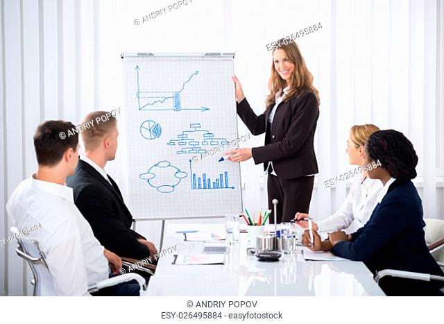 Group Of Businesspeople Looking At Confident Businesswoman Explaining In Presentation